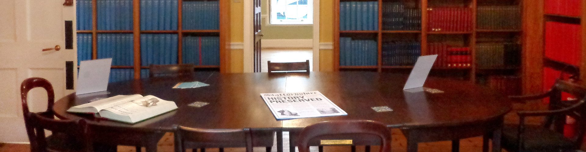 A view of a heritage room with a large dark wood table and bookshelves filled with large volumes.