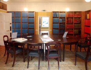 A view of a heritage room with a large dark wood table and bookshelves filled with large volumes.